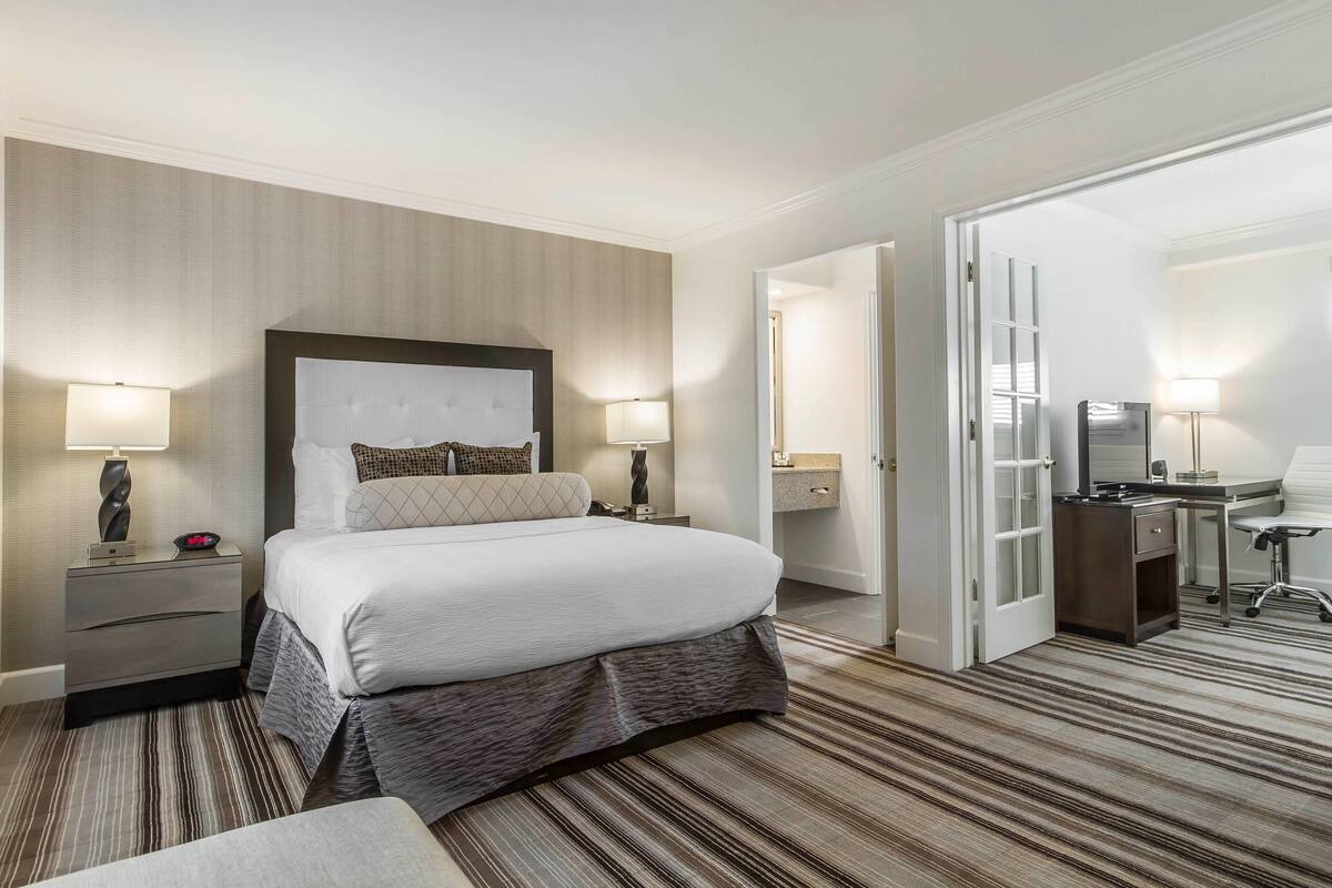 Une chambre d’hôtel avec un grand lit, deux tables de chevet avec des lampes, un bureau avec une chaise et une armoire.