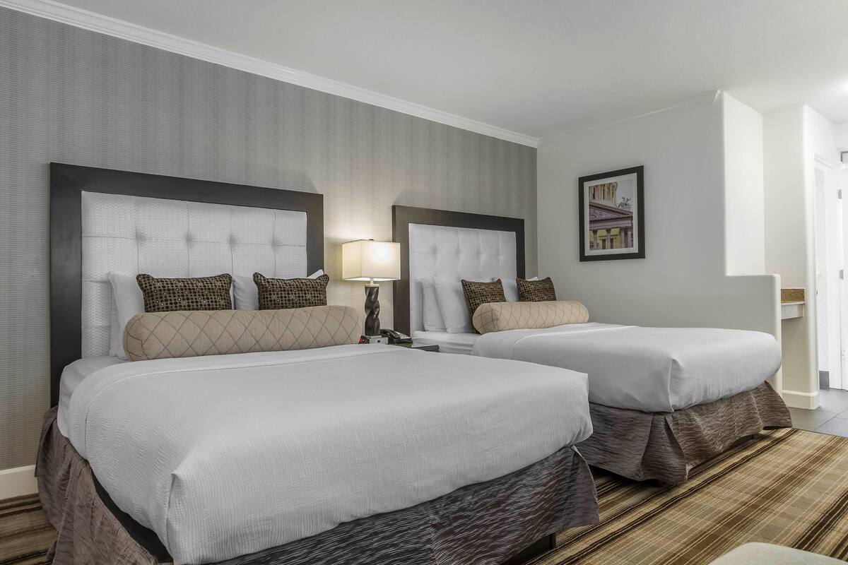 Une chambre d’hôtel avec deux lits, une grande fenêtre et un tableau encadré au mur.
