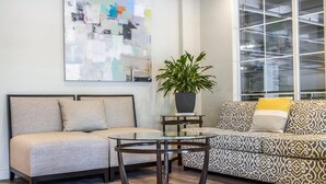 Ein Wohnzimmer mit einer Couch, einem Glastisch, einem gemusterten Sofa, einer Topfpflanze und einem großen abstrakten Gemälde an der Wand.