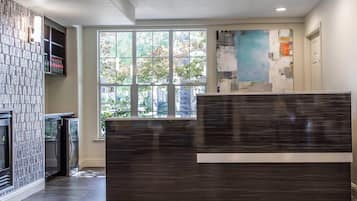 A modern reception area with a dark wood reception desk, a glass partition, and a large window offering a view of trees and buildings.