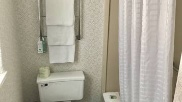 A bathroom with a toilet, a towel rack with multiple towels, a toilet paper holder, and a shower curtain.
