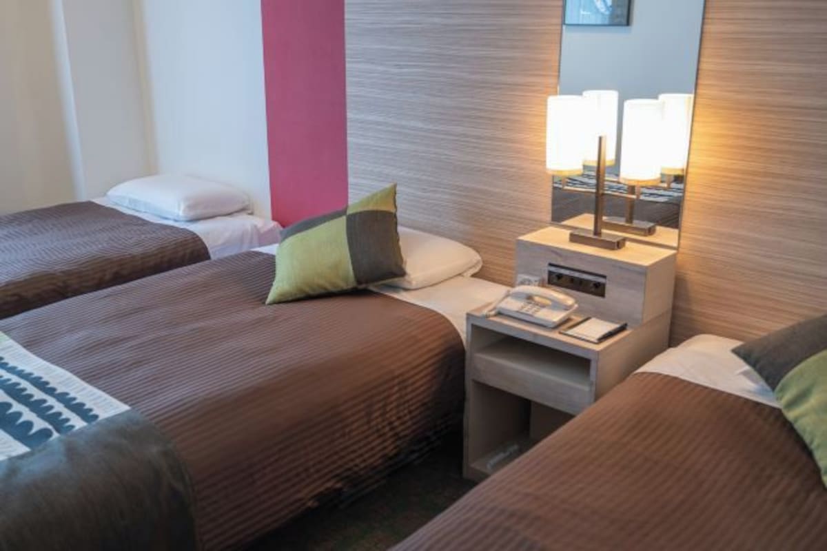 A hotel room with two beds, a nightstand with a lamp, and a mirror.