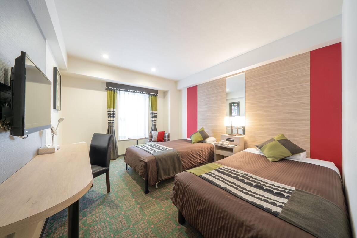A hotel room with two beds, a desk, a chair, a TV, and a large mirror.
