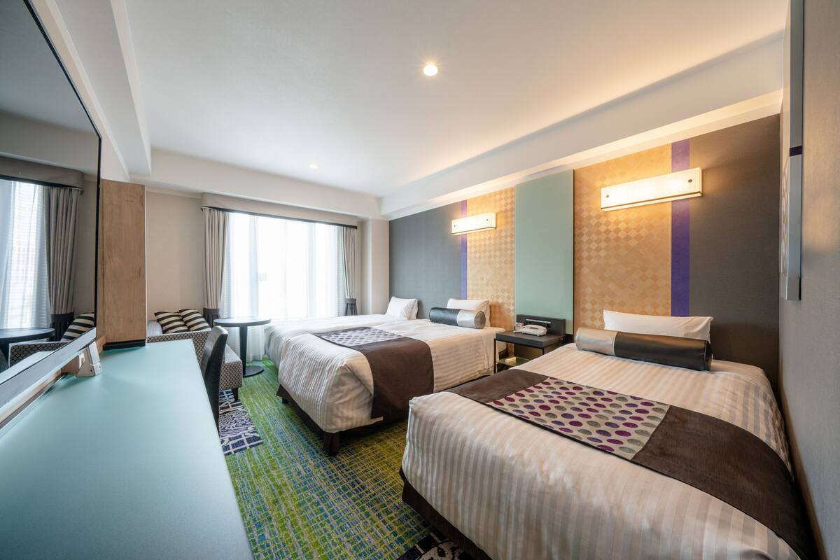 A hotel room with two beds, a desk, and a large mirror.