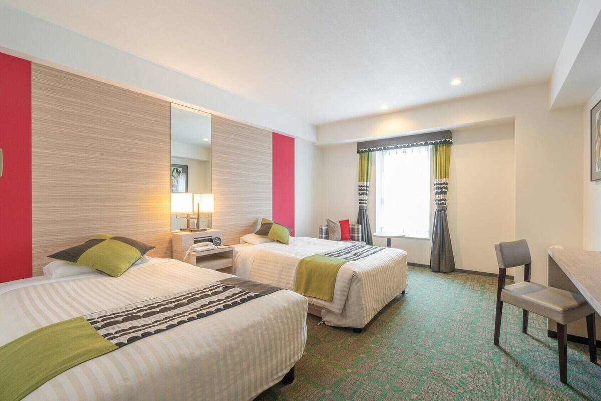 A hotel room with two beds, a desk, a chair, a television, and a window with curtains.