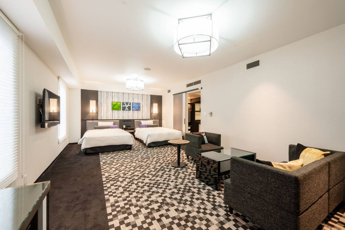 A hotel room with two beds, a sofa, a small table, and a TV.