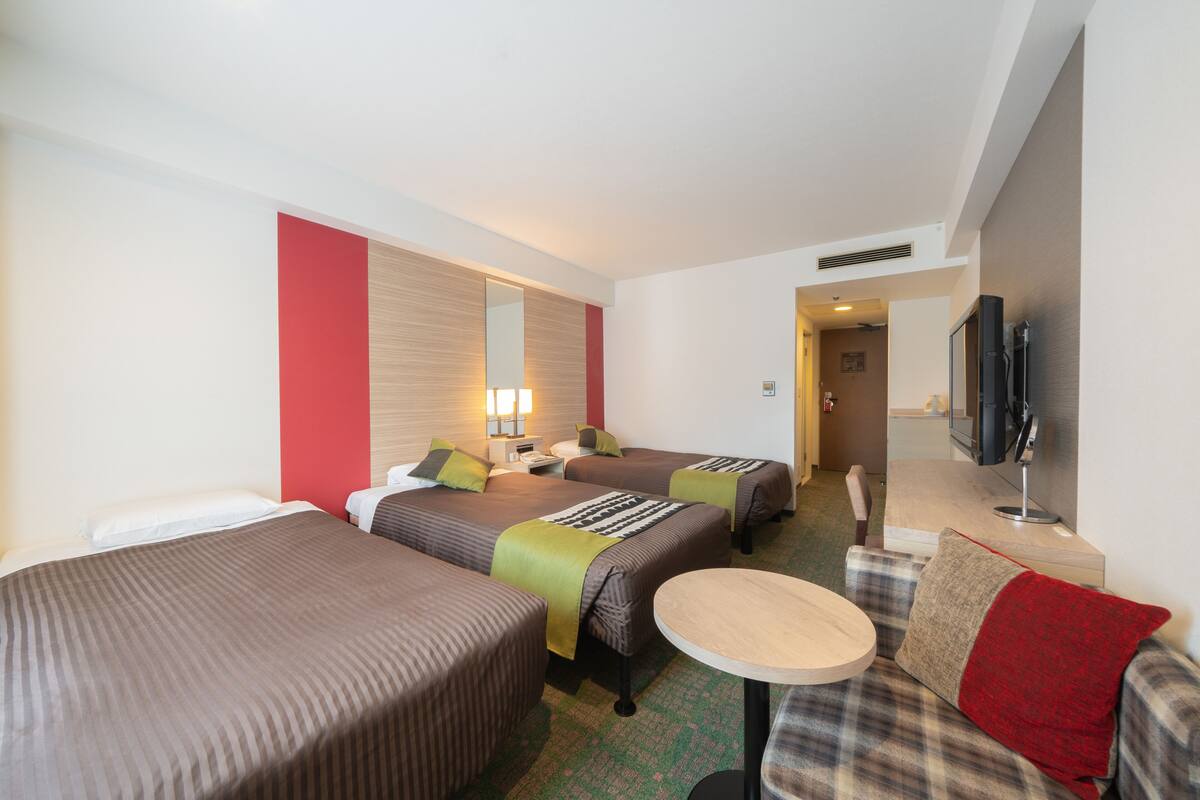 A hotel room with two beds, a small round table, a sofa, a TV, and a mirror.