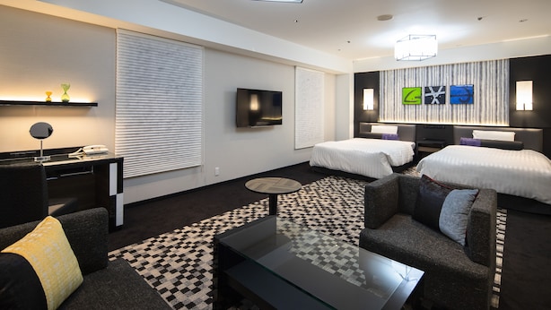 A modern hotel room with a checkered carpet, two beds, a sofa, a glass coffee table, and a TV on the wall. - New Otani Inn Sapporo (Sapporo)