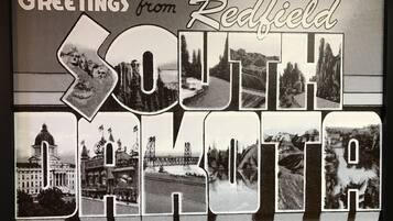 A framed greeting card with the text "Greetings from Redfield South Dakota" and various black and white photographs of landmarks and scenery.