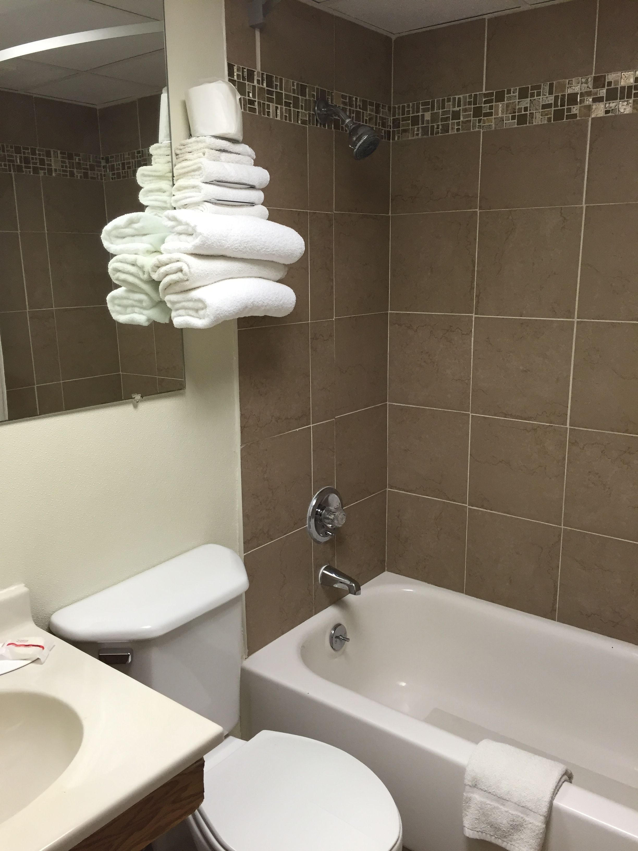 Un baño con inodoro, lavamanos y bañera. Hay una pila de toallas blancas colgadas en un perchero.