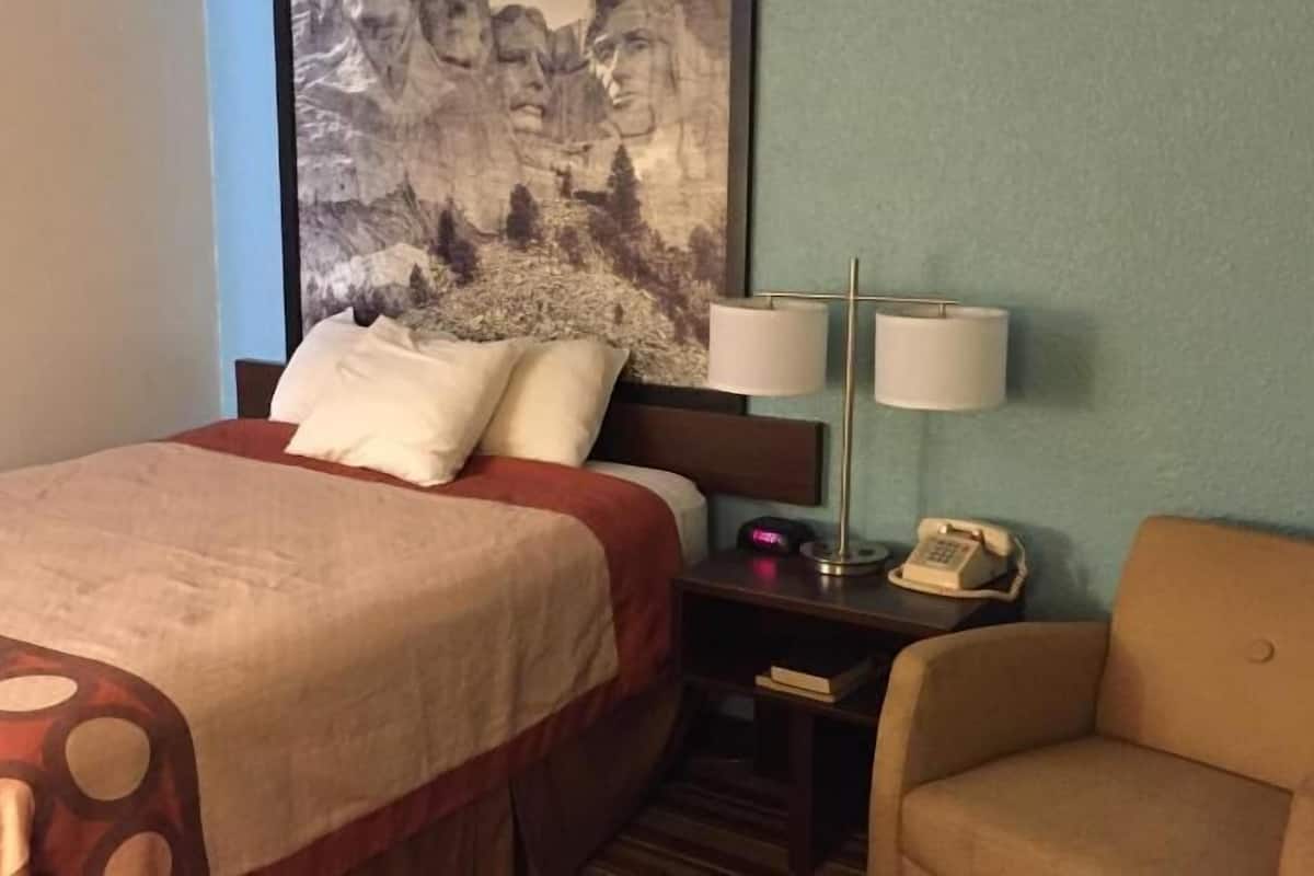 Hotelkamer met een bed, twee bedlampen, een stoel, nachtkastje met telefoon en een groot schilderij aan de muur.