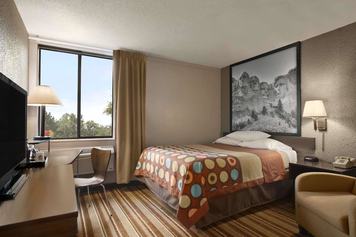 Een hotelkamer met een bed, een bureau, een stoel, een lamp en een schilderij aan de muur.