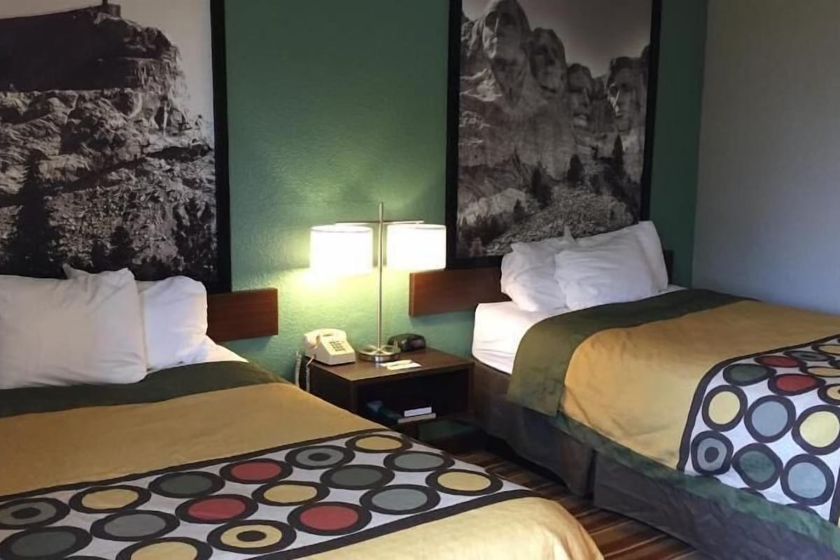 A hotel room with two beds, a nightstand with a lamp, and a telephone.