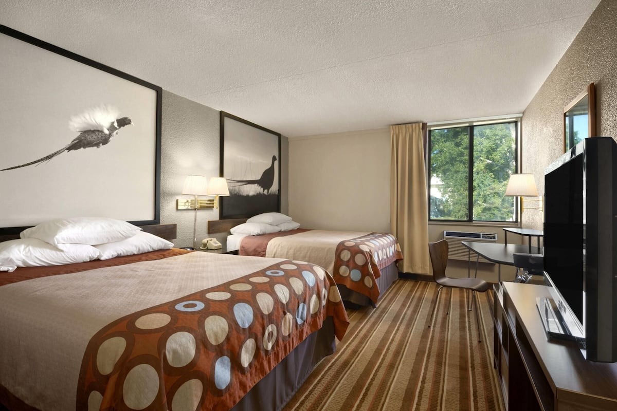 Een hotelkamer met twee bedden, een bureau, een televisie en kunstwerken aan de muur.