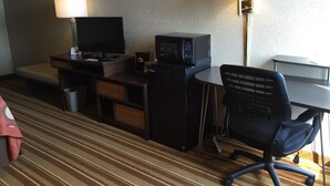 Ein Hotelzimmer mit Schreibtisch, Fernseher, Mikrowelle, Sessel und zwei Lampen.