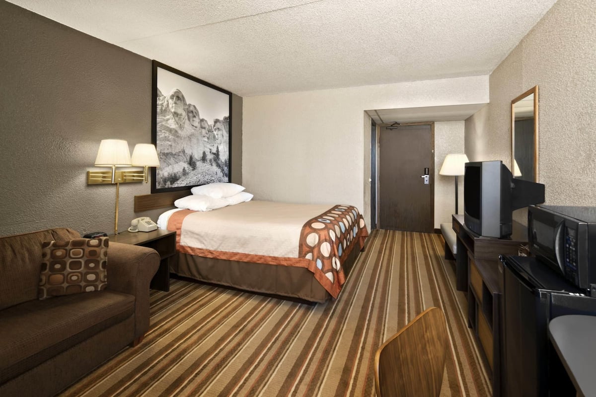 Een hotelkamer met een bed, een bank, een bureau met een televisie en een schilderij aan de muur.