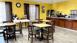 A dining area with wooden tables and chairs, a clock on the wall, and a kitchen area with appliances. - FairBridge Inn Express Mount Vernon (Mount Vernon)