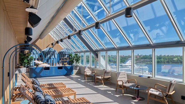 Un interior iluminado por el sol con un amplio techo de cristal, muebles de madera y vista a un crucero.