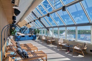A sunlit interior with a large glass ceiling, wooden furniture, and a view of a cruise ship. - Scandic Sodra Kajen (Stockholm)