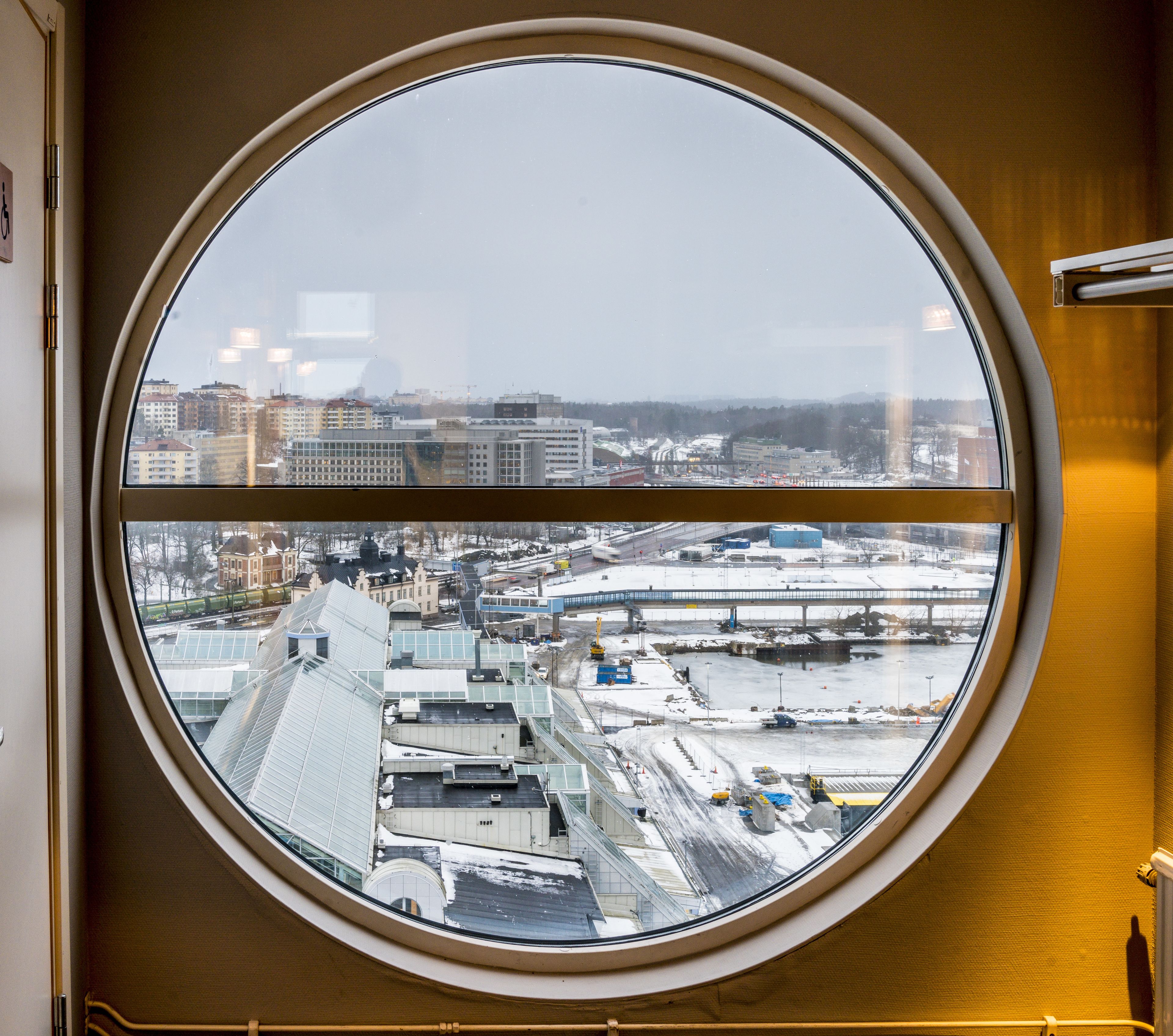 A round window with a view of a cityscape, including buildings and a bridge.