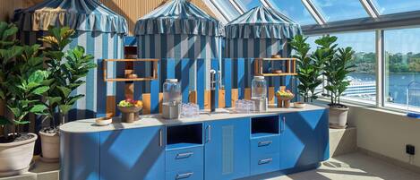 A modern kitchen with blue cabinets, a central island, and potted plants.