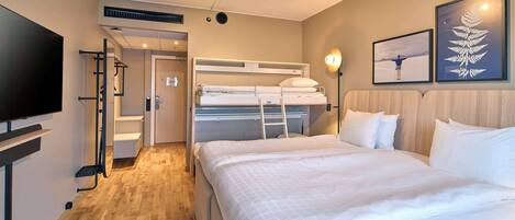 A hotel room with a bunk bed, a flat-screen TV, a wooden floor, and artwork on the walls.