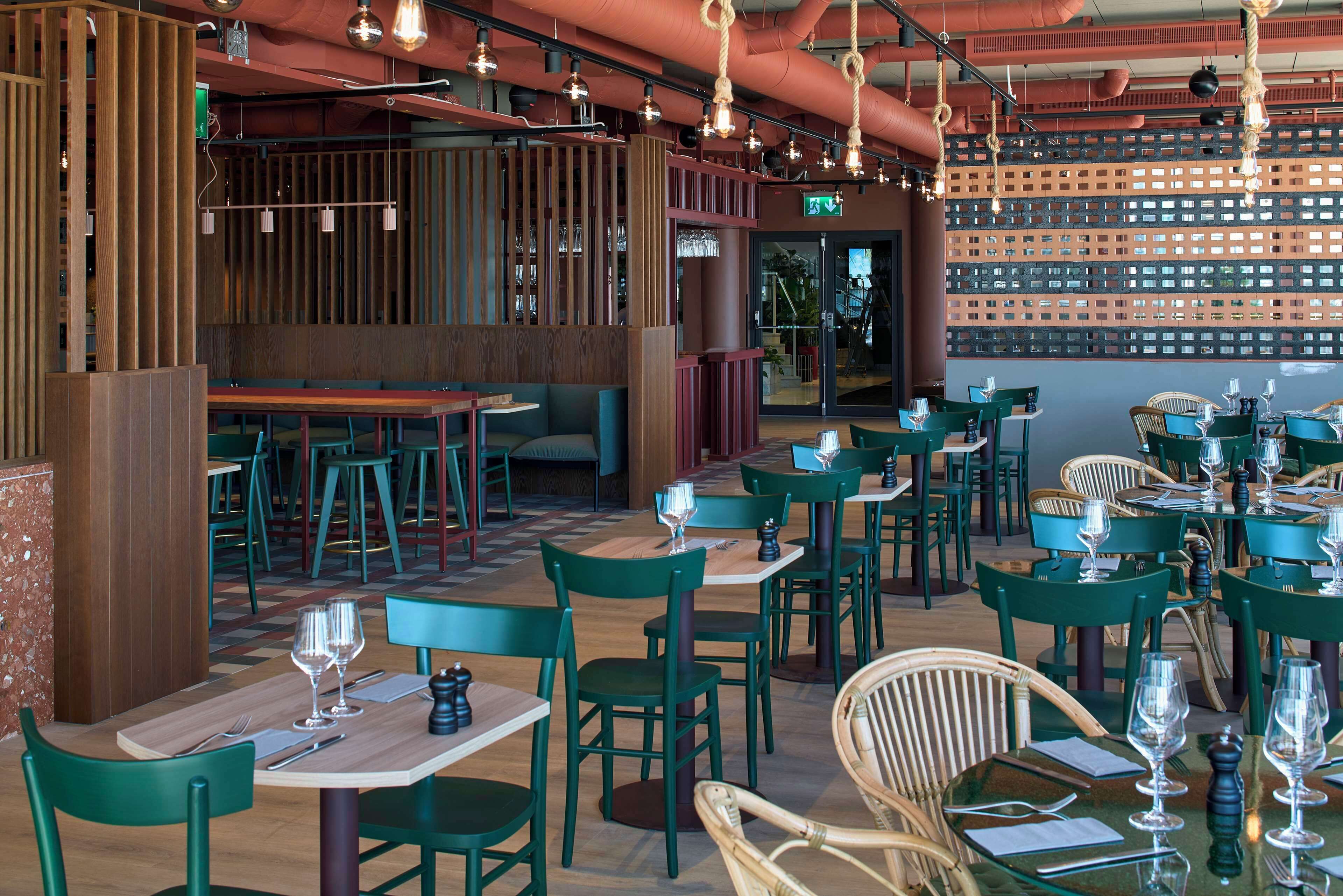A restaurant interior with green chairs, wooden tables, and hanging rope lights.