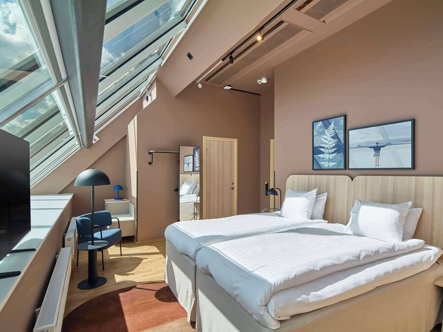 A modern hotel room with a large bed, a desk, a chair, and a TV.