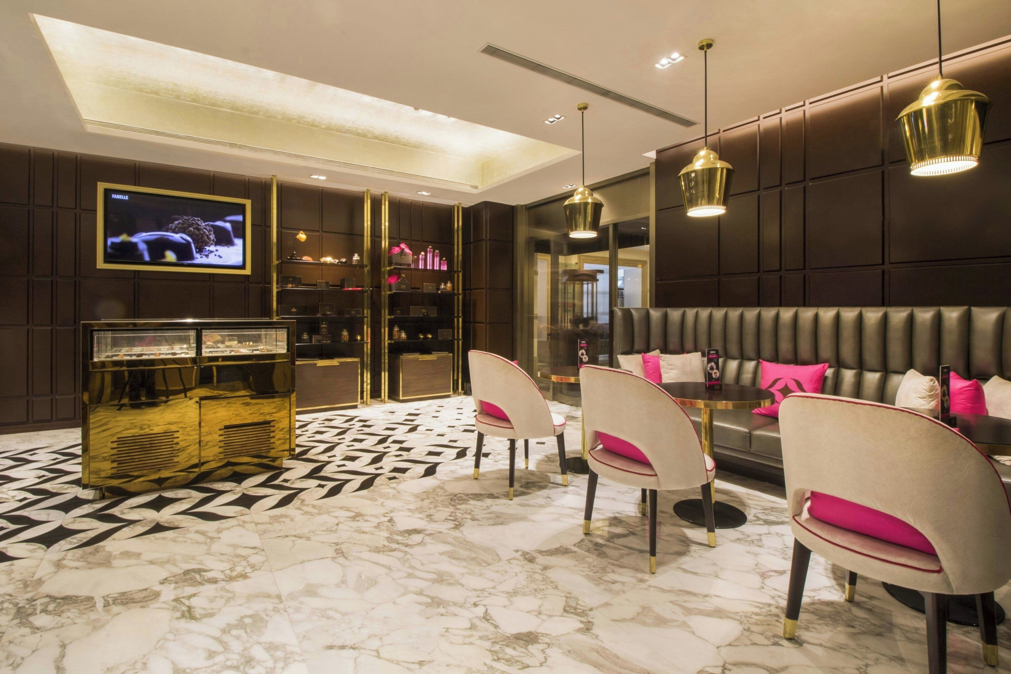 A modern interior with a marble floor, a seating area with cushioned chairs, a sofa with pink cushions, and pendant lighting.