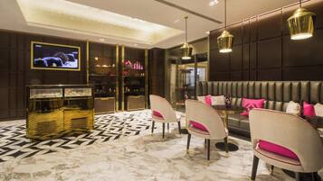 A modern interior with a marble floor, a seating area with cushioned chairs, a sofa with pink cushions, and pendant lighting.