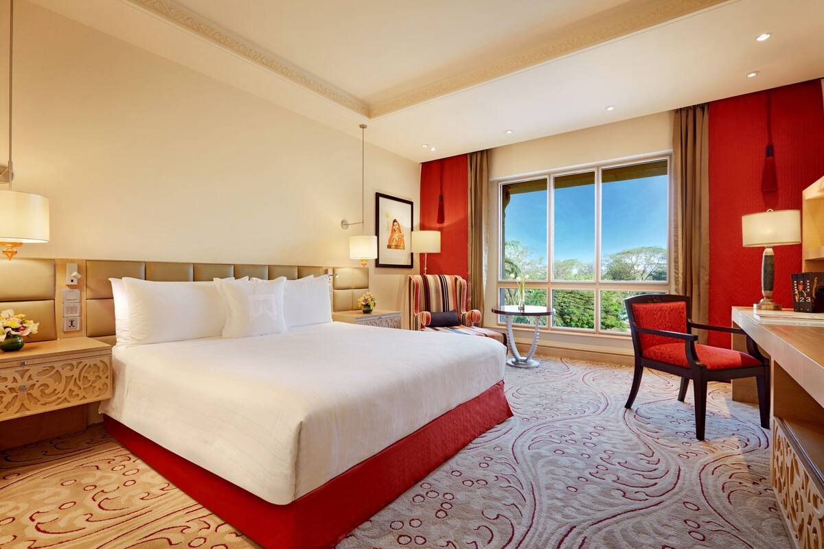 Ein Hotelzimmer mit einem großen Bett, einem Schreibtisch mit Stuhl, einem Fenster mit Aussicht und einer roten Akzentwand.