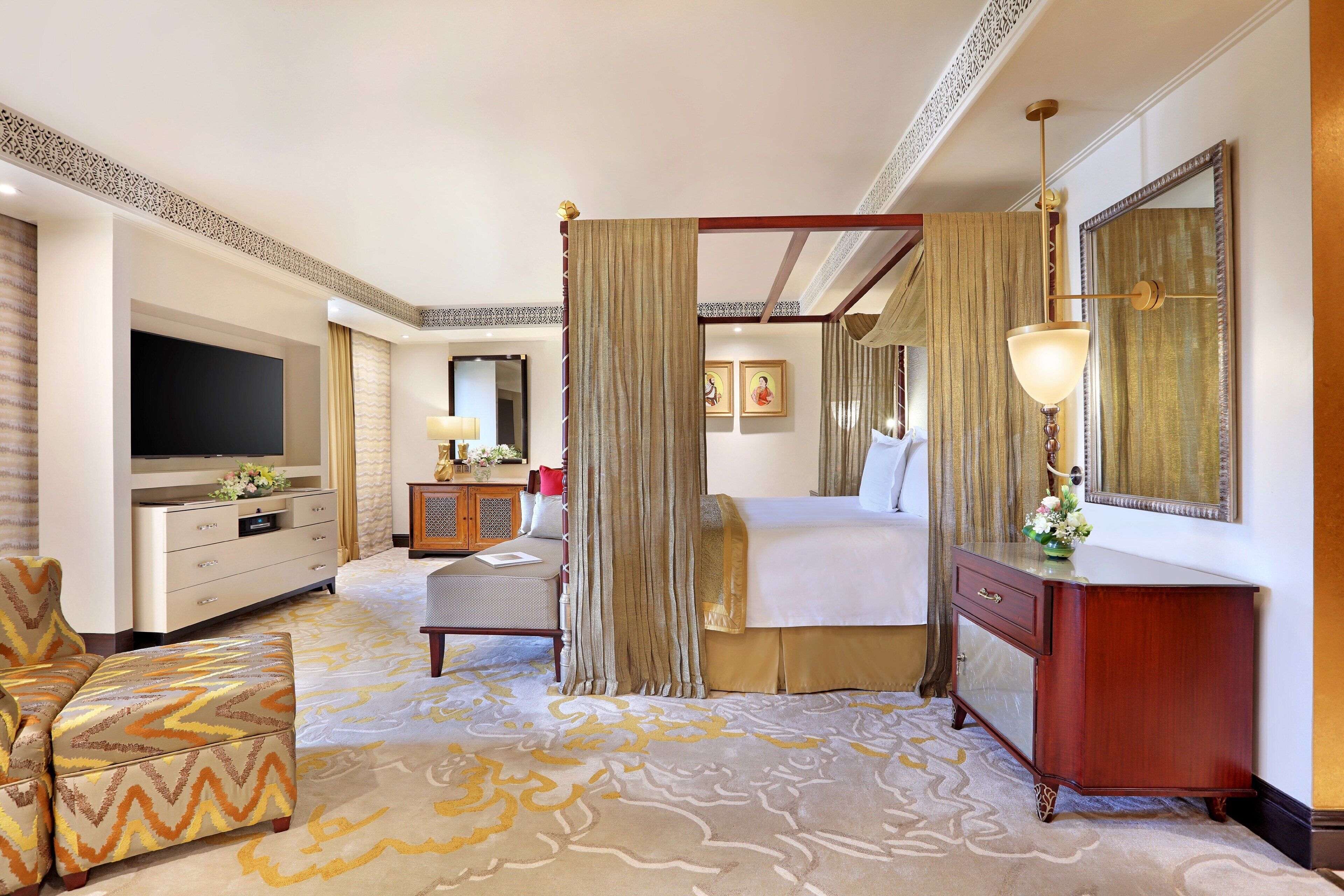 A hotel room with a four-poster bed, a television, a desk, and a chair.