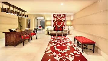 A hotel lobby with a red carpet, a reception desk, seating area, and a staircase.