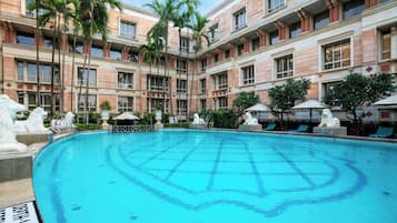 Piscina de hotel com água azul cristalina, rodeada por palmeiras e estátuas.