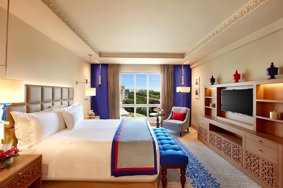 Ein Hotelzimmer mit einem großen Bett, einem Fernseher, einem Schreibtisch und Blick ins Freie.