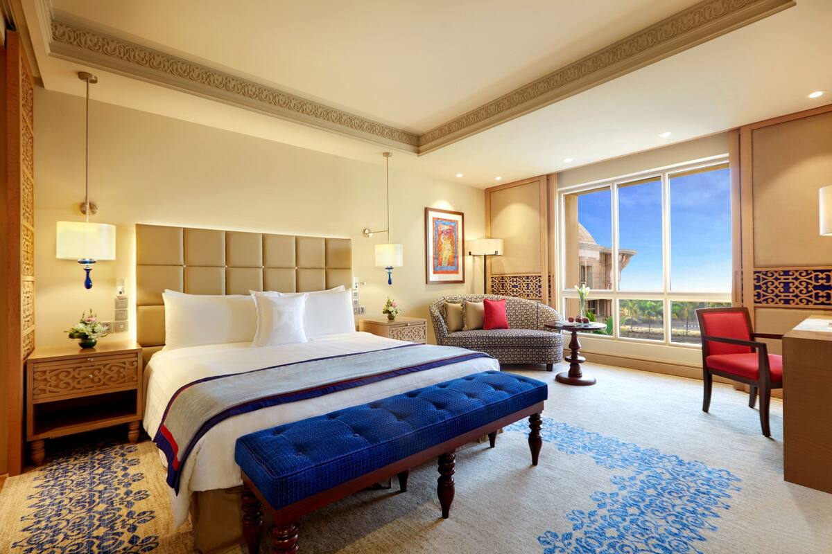 Ein Hotelzimmer mit einem großen Bett, einer Bank, einem Schreibtisch und Blick ins Freie.