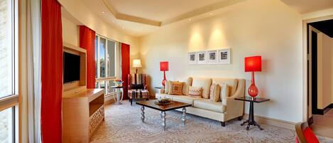 A spacious living room with a large flat-screen TV, a sofa set, a coffee table, and red lamps.