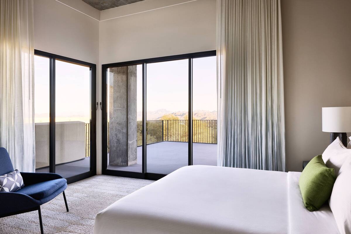 Ett hotellrum med en stor säng, en stol och en balkong med utsikt över bergen.