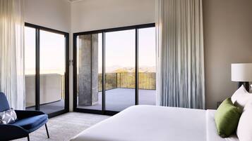 A hotel room with a large bed, a chair, and a balcony with a view of the mountains.