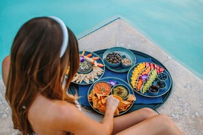 A person sitting by a poolside with a tray of snacks and dips.