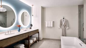 A modern bathroom with a large mirror, two sinks, a vanity with shelves, a bathtub, and a robe hanging on the wall.