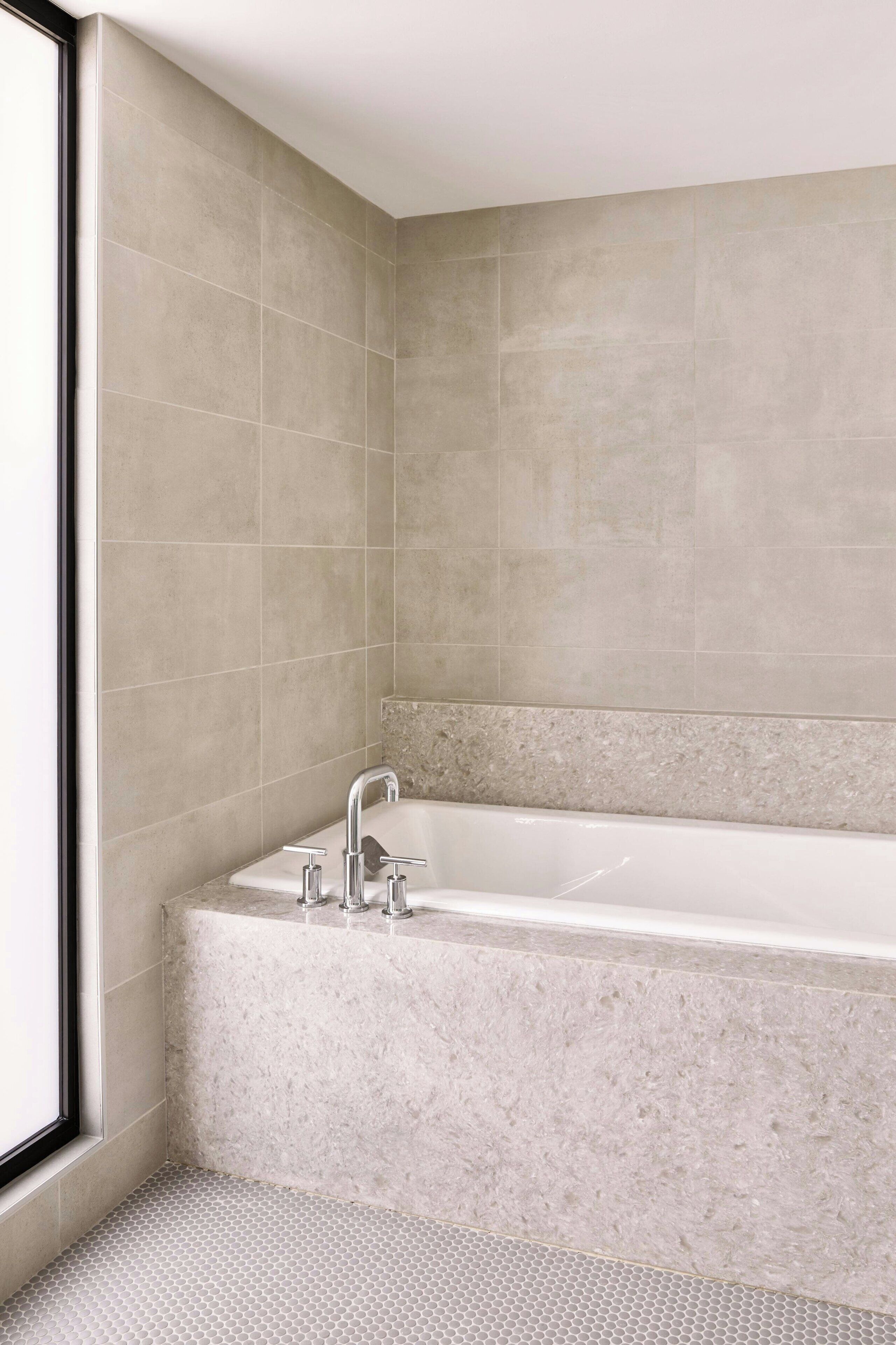 Un baño moderno con una bañera independiente, paredes con azulejos y un ventanal que proporciona luz natural.