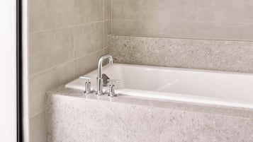 Un baño moderno con una bañera independiente, paredes con azulejos y un ventanal que proporciona luz natural.
