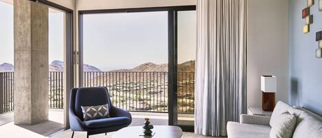 A modern hotel room with a balcony, a sofa, a chair, and a small table.