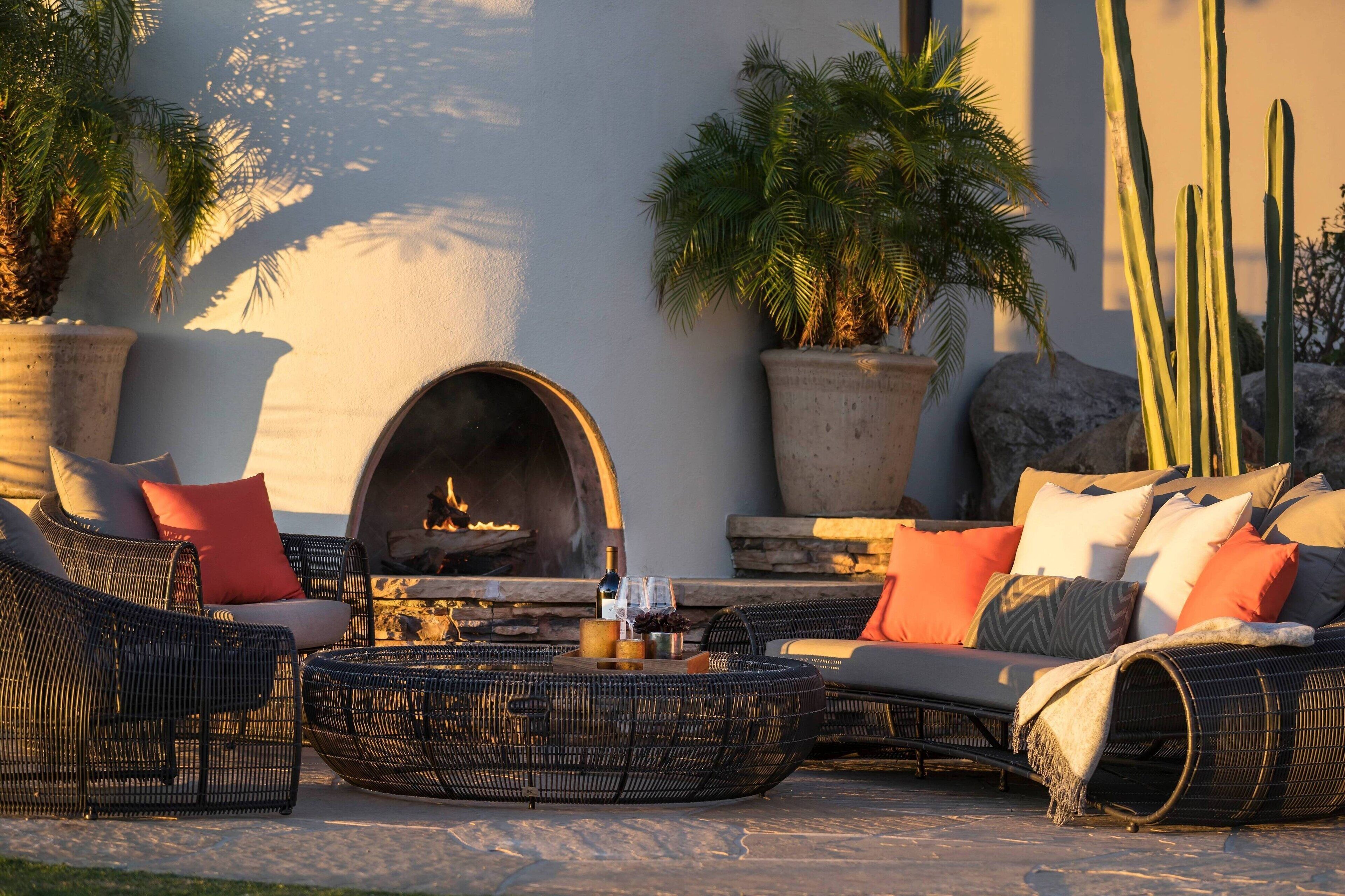 An outdoor seating area with wicker furniture, a stone fireplace, and potted plants.