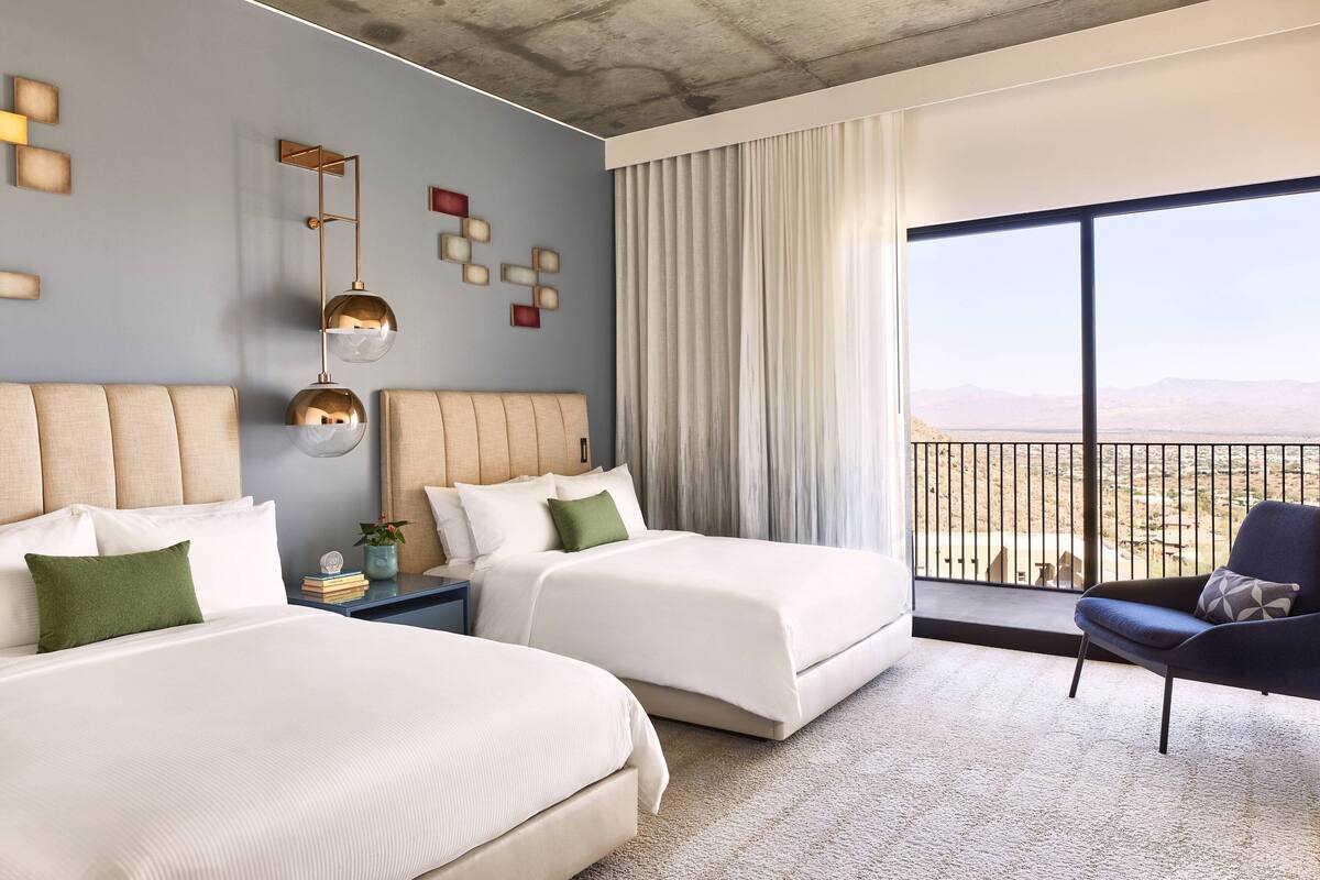 Ett hotellrum med två sängar, ett stort fönster med utsikt, en modern kristallkrona och en balkong med räcke.