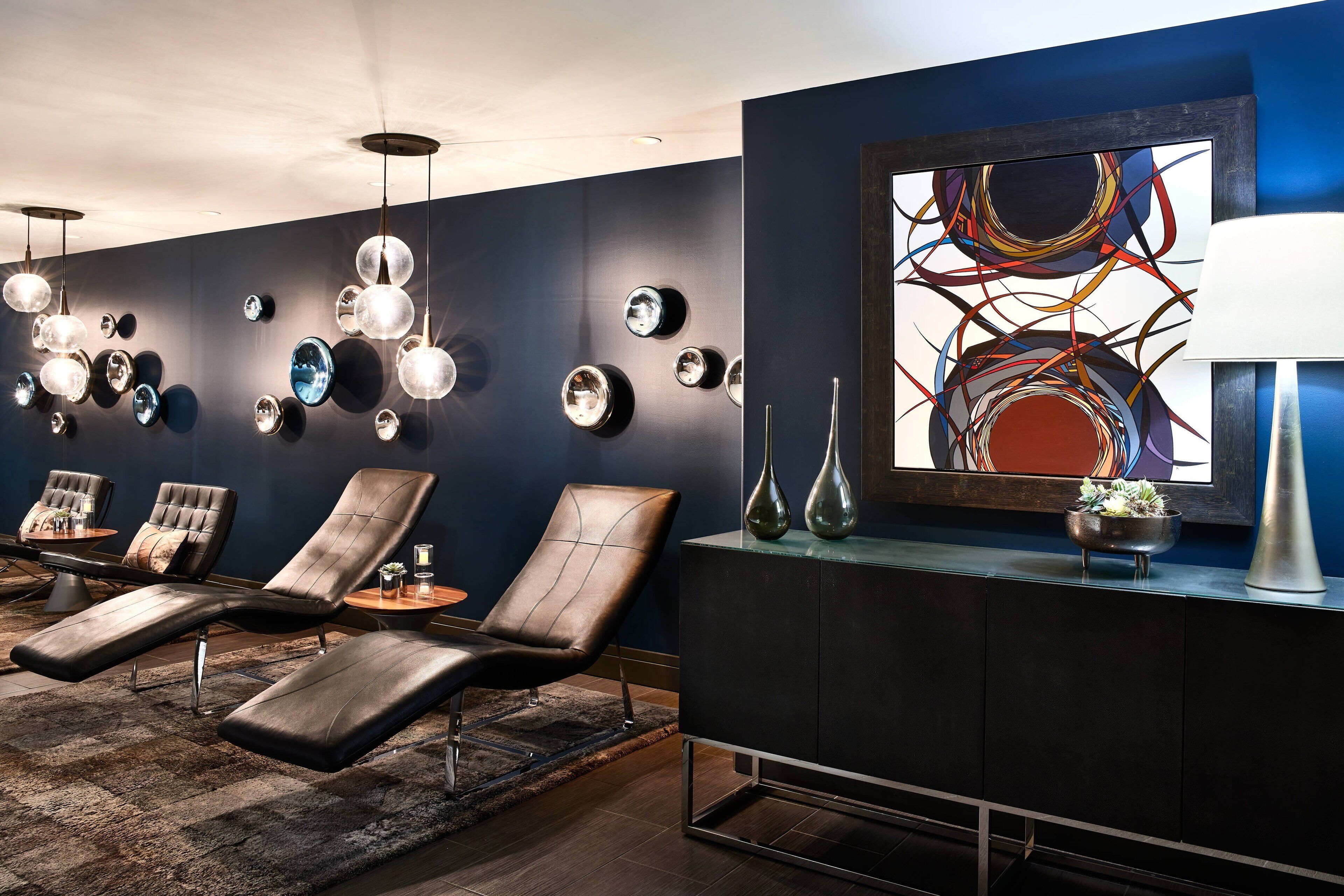 A modern lounge area with reclining chairs, a dark wall with circular mirrors, and a contemporary abstract painting.