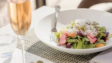 A white plate with a salad, a glass of wine, and a fork on a table with a woven placemat.