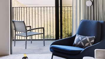 Habitación con vista a un paisaje desértico a través de una puerta corrediza de vidrio. Hay un sillón azul con un cojín de diseño, una mesa de centro de madera con una pila de piedras y un sofá blanco.