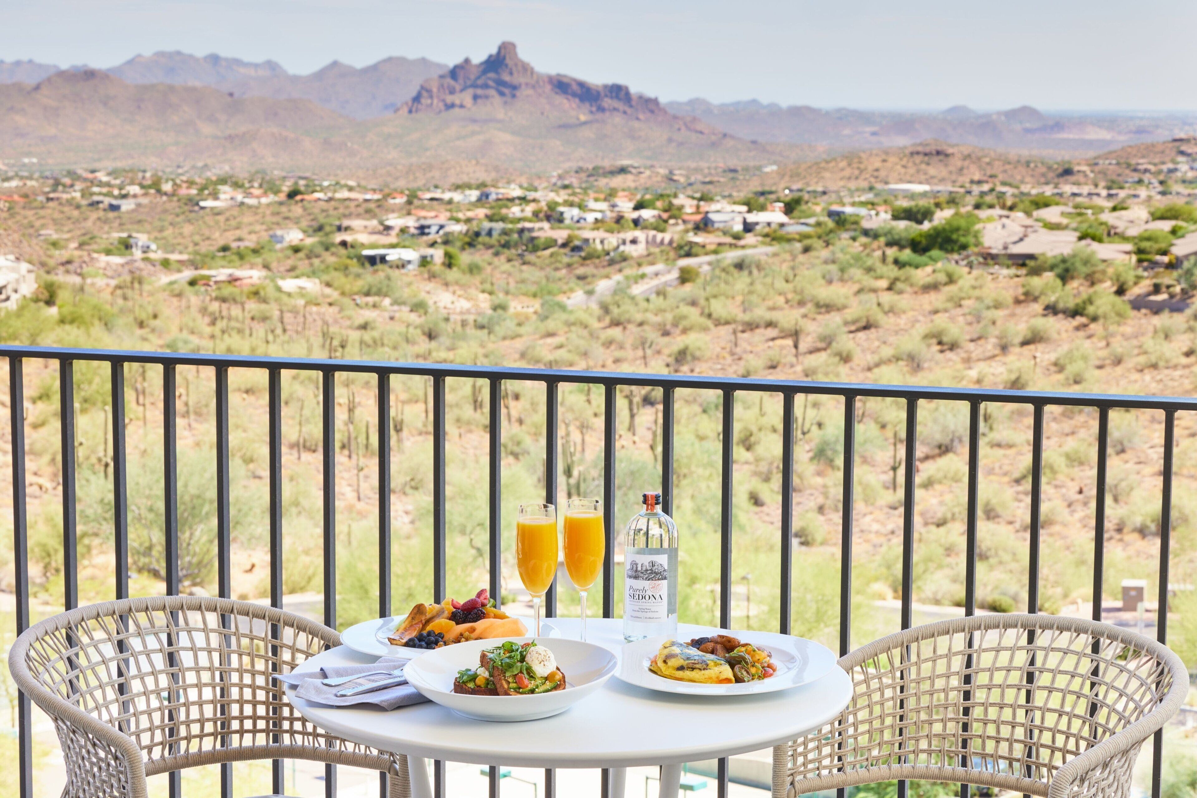 A balcony with a table set for breakfast, overlooking a desert landscape with mountains in the distance.